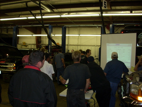 A class gathered around a screen beside a truck in a shop bay