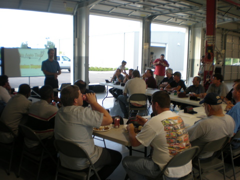 A class at tables in an open shop, the instructor at the screen